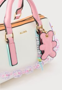 Bolso blanco texturizado con correas rosas, detalles de cremallera naranja y accesorios de encanto coloridos que incluyen un oso rosa y cuentas con letras.