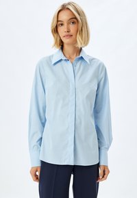 Camicia azzurra chiara con colletto a punte, maniche lunghe e orlo dritto. Realizzata in tessuto morbido. Presenta un design minimalista.