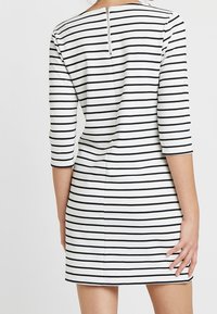 Raidallinen mekko, jossa kolme neljänneksen hihaa, mustavalkoiset vaakaraidat, vartalonmyötäinen malli ja selässä vetoketjukiinnitys.