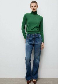 Pulover verde cu guler înalt și croială strâmtă, asortat cu blugi evazați bleu deschis. Pantofii sunt maro, cu vârf ascuțit. Design simplu și casual.