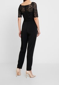 Top de encaje negro con mangas cortas combinado con pantalones ajustados negros. Acentuado con zapatos de tacón altos en color nude. Color sólido, textura suave.