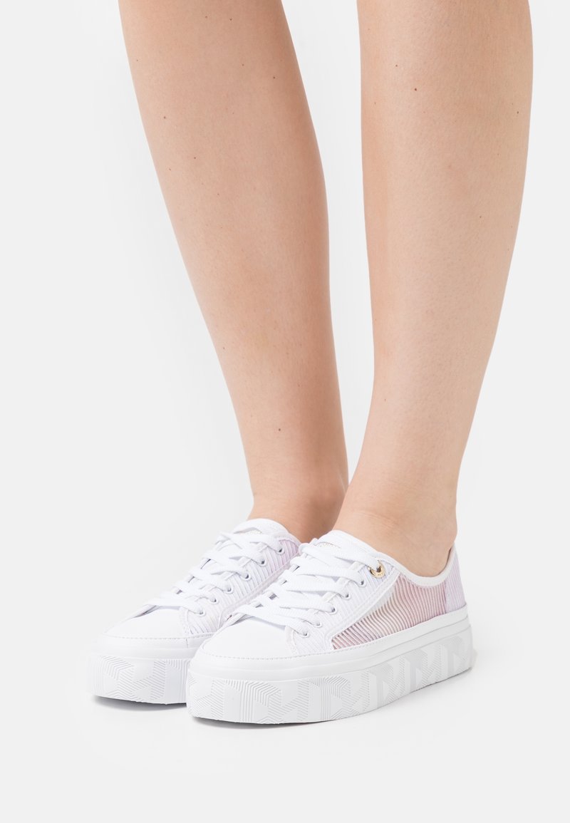 Baskets blanches à plateforme avec côtés en mesh, portées pieds nus sur un fond clair uni.