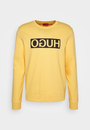 Sweat-shirt jaune à manches longues avec un bloc rectangulaire noir et un texte « HUGO » inversé sur la poitrine, col rond, poignets et ourlet côtelés.