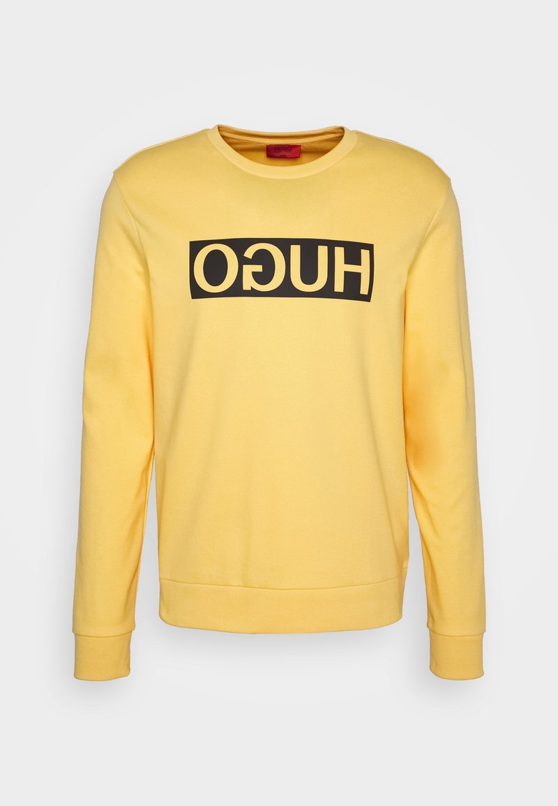 Sweat-shirt jaune à manches longues avec un bloc rectangulaire noir et un texte « HUGO » inversé sur la poitrine, col rond, poignets et ourlet côtelés.