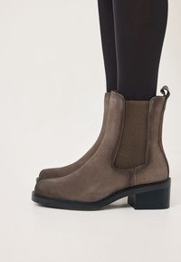 Botas de tobillo de ante marrón con paneles laterales elásticos y un tacón bajo. Punta redondeada y lengüeta en la parte trasera para un fácil calzado.