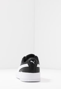 Black and white sneaker with a textured leather upper, rubber sole, and a logo on the back. Low-top design with padded collar.