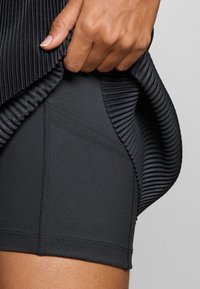 Pantalones cortos deportivos negros con un tejido suave, detalle de costura lateral y un superpuesto plisado y texturizado. La vista de cerca destaca la construcción.