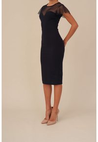 Marinblå knälång klänning med genomskinliga korta ärmar och figursydd silhuett. Slät tyg med en lätt glans. Bärs med nude högklackade skor.