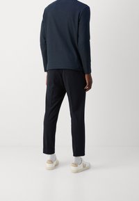 Marynarska koszula z długim rękawem w połączeniu z czarnymi spodniami i białymi trampkami z brązowymi akcentami. Prosty, minimalistyczny design z luźnym krojem.