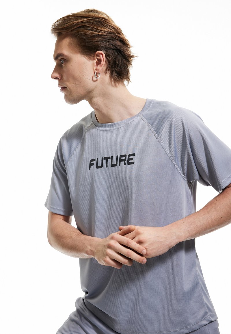 Camiseta atlética de color gris claro con un tejido texturizado, que presenta la palabra "FUTURO" en letras negras en negrita a lo largo del pecho y un escote redondo.