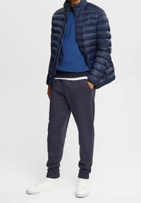 Marinblå pufferjacka, blå stickad tröja, mörkgrå joggers och vita sneakers. Släta texturer med kviltad design på jackan.