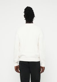 Weißer gestrickter Pullover mit lockerer Passform, gerippten Bündchen und Saum. Das Design verfügt über einen v-förmigen Rückenausschnitt und nahtlose Schultern.