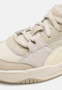 Beige sportcipők, amelyek textil és velúr anyagok keverékéből készültek, kerek orral, párnázott nyelvvel és bonyolult fűzéssel, erősített fűzőlyukakkal.