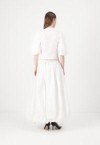 Blusa bianca con maniche a palloncino abbinata a una lunga gonna bianca fluida, con vita elasticizzata e scarpe nere con tacco alto. Tessuto dalla superficie liscia.