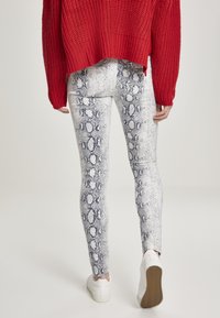 Leggings blancs avec un motif de peau de serpent bleue, associés à un gros pull en tricot rouge et des baskets blanches. La tenue présente une coupe décontractée.