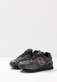 Schwarze und graue Sneakers mit einer strukturierten Oberseite, gepolsterter Sohle und hervorgehobenem Seitenlogo. Die Schnürsenkel sind schwarz mit kontrastierenden Akzenten.