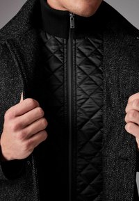 Palton din amestec de lână cu un model in dungi în zig-zag, fermoar frontal și căptușeală interioară din nailon negru matlasat. Prezintă un guler și mansete cu model canelat.