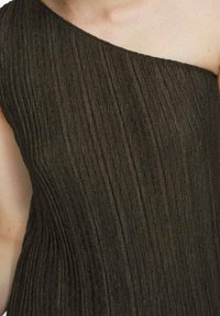 Haut asymétrique vert olive foncé ; tissu texturé avec plis verticaux, design à une épaule, et finition lisse.