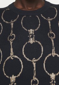 Pletený svetr s tmavě modrým základem a vzorem z kovově zlatých řetízkových článků, kulatým výstřihem a texturovanou látkou.