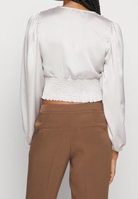 Silk blouse in light gray with a smocked white waist. Long puff sleeves and a round neckline, paired with brown tailored pants.