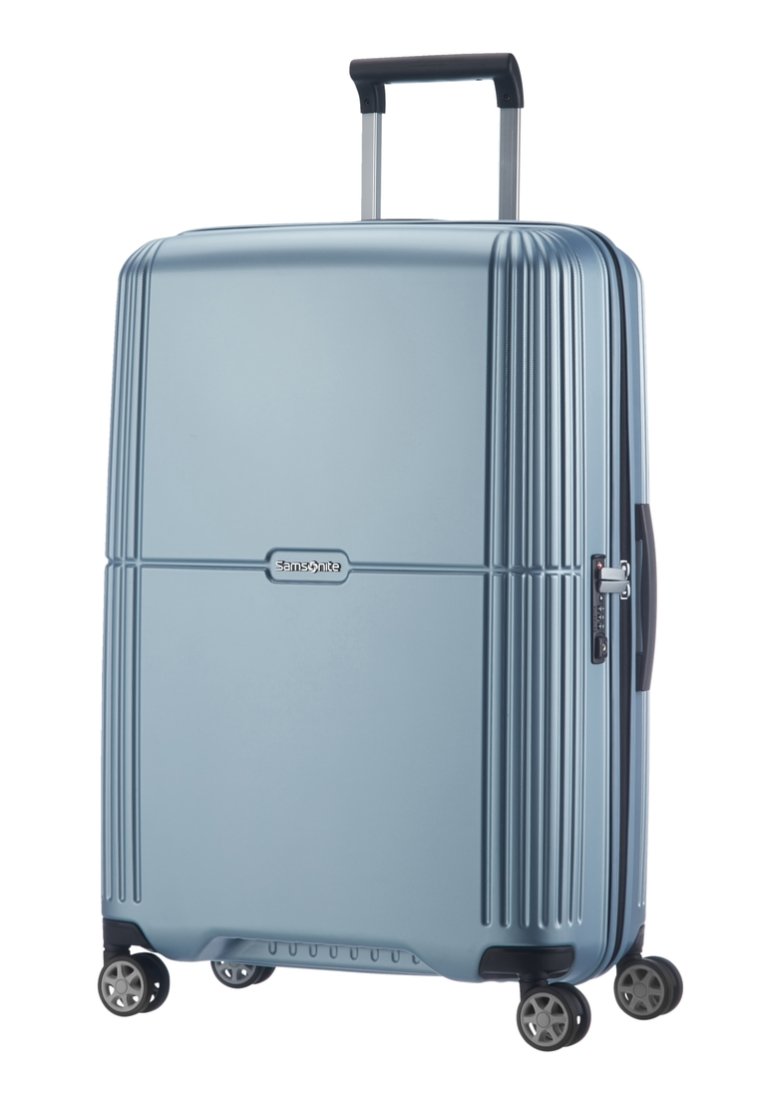 Valise rigide de couleur bleu clair, avec des rainures verticales, une poignée rétractable et quatre roues pivotantes pour une mobilité facile.