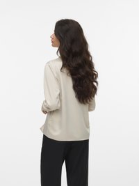 Lange mouwen, beige blouse met een gladde, satijnen textuur; rechte snit en lichte draping aan de achterkant, gecombineerd met zwarte broek.