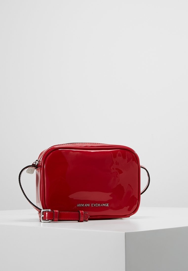 Czerwona torebka crossbody z lakierowanej skóry w kształcie prostokąta, z srebrnym logo i regulowanym paskiem. Gładka faktura z błyszczącym wykończeniem.