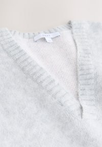 Pull en maille gris clair doux avec un col en V côtelé et une étiquette blanche indiquant "NEXT" à l'encolure.