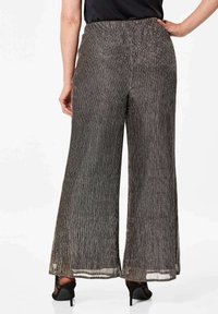 Wijdvallende broek van metallic zwarte stof, met verticale strepen, een elastische tailleband en een vloeiende silhouet. Achteraanzicht zichtbaar.