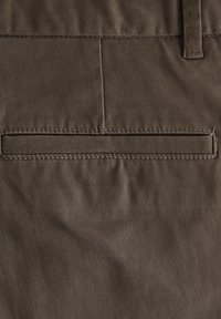 Brun bomuldsstof med en glat tekstur, der har en paspoleret lomme og en pæn syning langs kanterne. Minimalistisk design og funktionelt detalje.