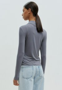 Langsleeve, getailleerd shirt in een zachte grijze stof met een kraag, gedragen met lichtgewassen denim jeans, getoond vanaf de achterkant.