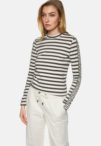 Gestreiftes Langarmtop in Grau und Weiß, mit gerafftem Detail an den Ärmeln, kombiniert mit weißen Hose mit elastischem Bund.