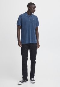 Marineblå polo skjorte laget av myk bomull, med krage og placket med tre knapper. Kombinert med svarte bukser og svarte sneakers.