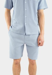 Ljusblå, rippad kortärmad skjorta med knappar och bröstficka, kombinerad med matchande rippade shorts, båda i mjukt tyg.