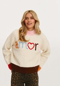 Biały sweter z teksturowanym wzorem w jodełkę, z kolorowymi haftowanymi literami "amore" oraz kontrastowymi ściągaczami w kolorze brązowym i różowym.