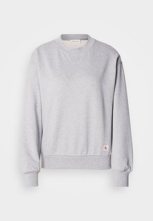 Sivý bavlnený sveter s kulatým výstrihom, rebrovanými manžetami a pásikom. Obsahuje malú nášivku s logom na spodnej strane. Hladká textúra.