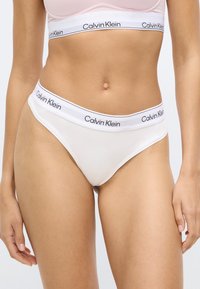 Λευκό βαμβακερό στρινγκ με χαμηλή μέση, με μαύρο λογότυπο Calvin Klein στη μέση. Λεία υφή, μινιμαλιστικό σχήμα.