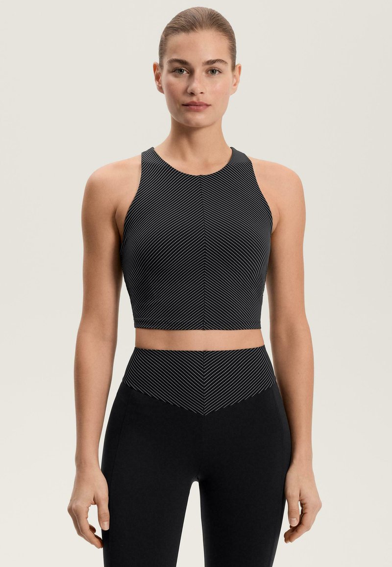 Čierny crop top s bielymi diagonálnymi pruhmi, s vysokým golierom a priliehavým strihom. Kombinovaný s čiernymi legínami s vysokým pásom.