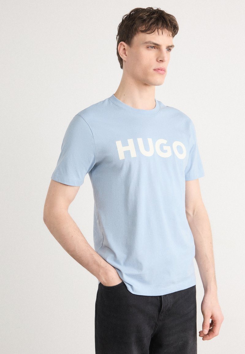Fénykék pamut póló kerek nyakkivágással és rövid ujjakkal, elöl nagy fehér betűkkel a "HUGO" felirattal.