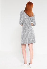 Grå och vit mönstrad klänning med trekvartslånga ärmar, A-linjeform och mjuk textur. Bärs med vita sneakers, sedd bakifrån.