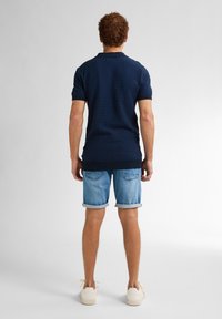 Námořnická polokošile s texturovaným vzorem, spárovaná se světle modrými denimovými šortkami. Bílé tenisky dokončují ležérní outfit.