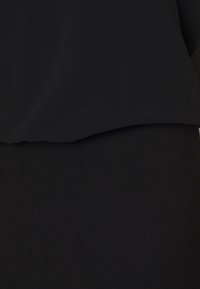 Zwarte top met een zachte, gladde textuur, met een losse pasvorm en een licht gebogen zoomlijn die over een bijpassende zwarte rok valt.