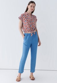 Blommönstrad kortärmad skjorta med knuten framsida, matchad med ljusblå skräddarsydda byxor och vävda beige sandaler. Slät tygkvalitet.