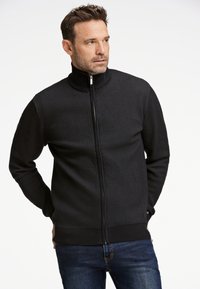 Sort zip-up jakke med høj krave, tekstureret stof, ribbede manchetter og søm. Har et subtilt diamantmønster overalt.