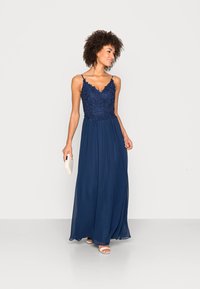Marinblå maxi-klänning med spetsbodice, V-ringning och tunna axelband. Flödande kjol i lätt material. Kombinerad med en clutch och sandaler.