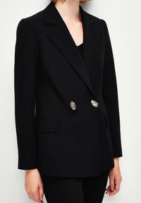 Černý dvouřadý blazer vyrobený z hladkého materiálu, s klopovými límci a kovovými knoflíky, bočními kapsami a přizpůsobeným střihem.