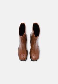 Brown, glossy leather ankle boots with a fitted design and rounded toes, featuring black soles and a smooth texture.