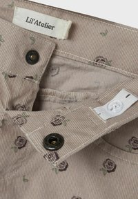 Tessuto a righe beige con piccoli motivi di rose viola scuro. Presenta bottoni neri e bianchi, con un'etichetta in tessuto che reca la scritta "Lil'Atelier."