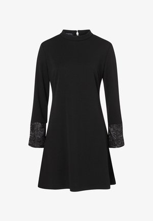 Robe noire à manches longues, avec un col montant et des accents en dentelle sur les poignets. Confectionnée dans un tissu lisse, design à mi-genoux.