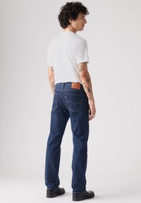 Jeans de denim azul con corte recto, que presentan una marca de parche en el bolsillo trasero y un diseño clásico de cinco bolsillos.
